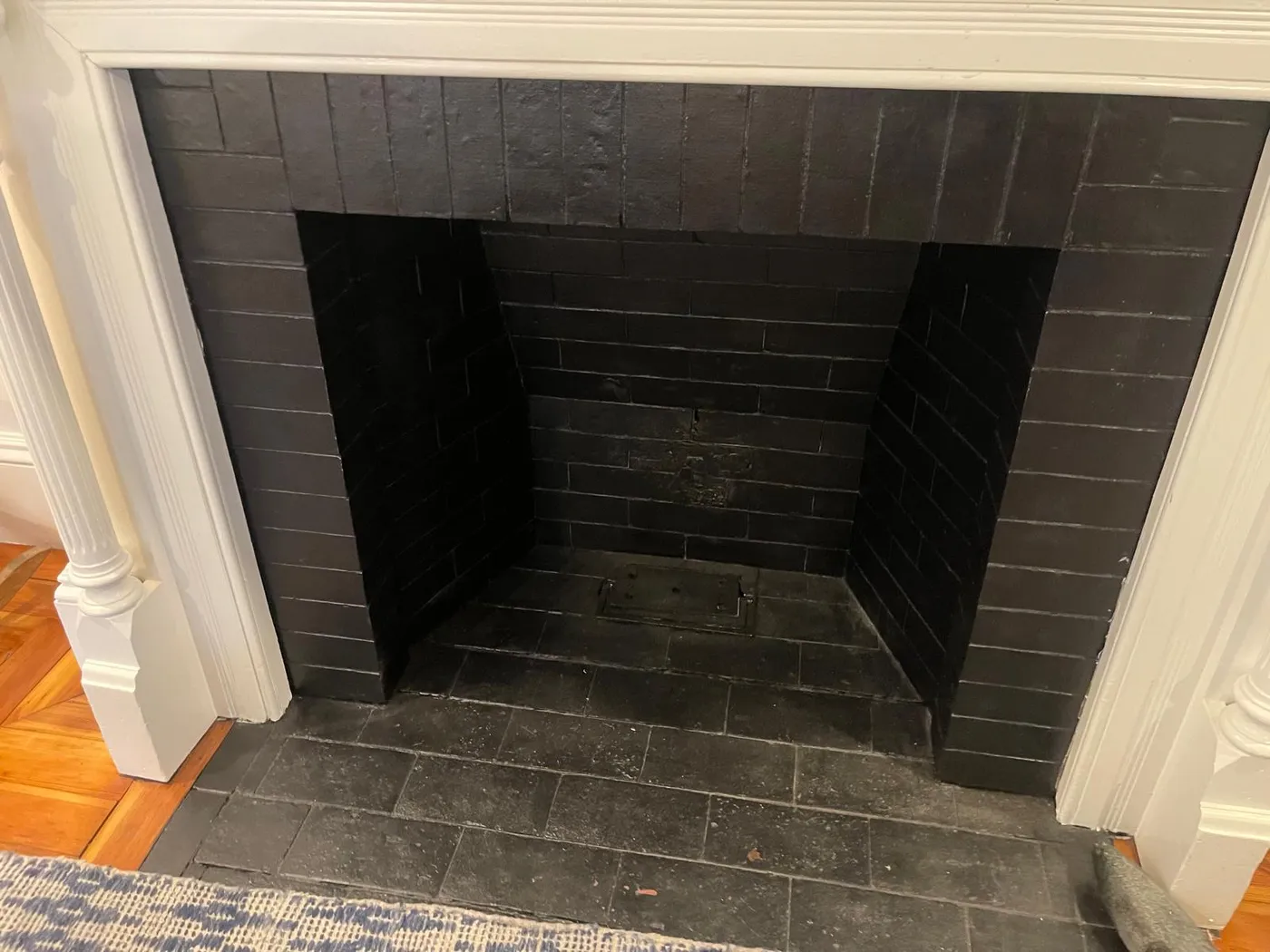 Restored fireplace with black-painted brick firebox, white wood mantel surround, and dark stone hearth