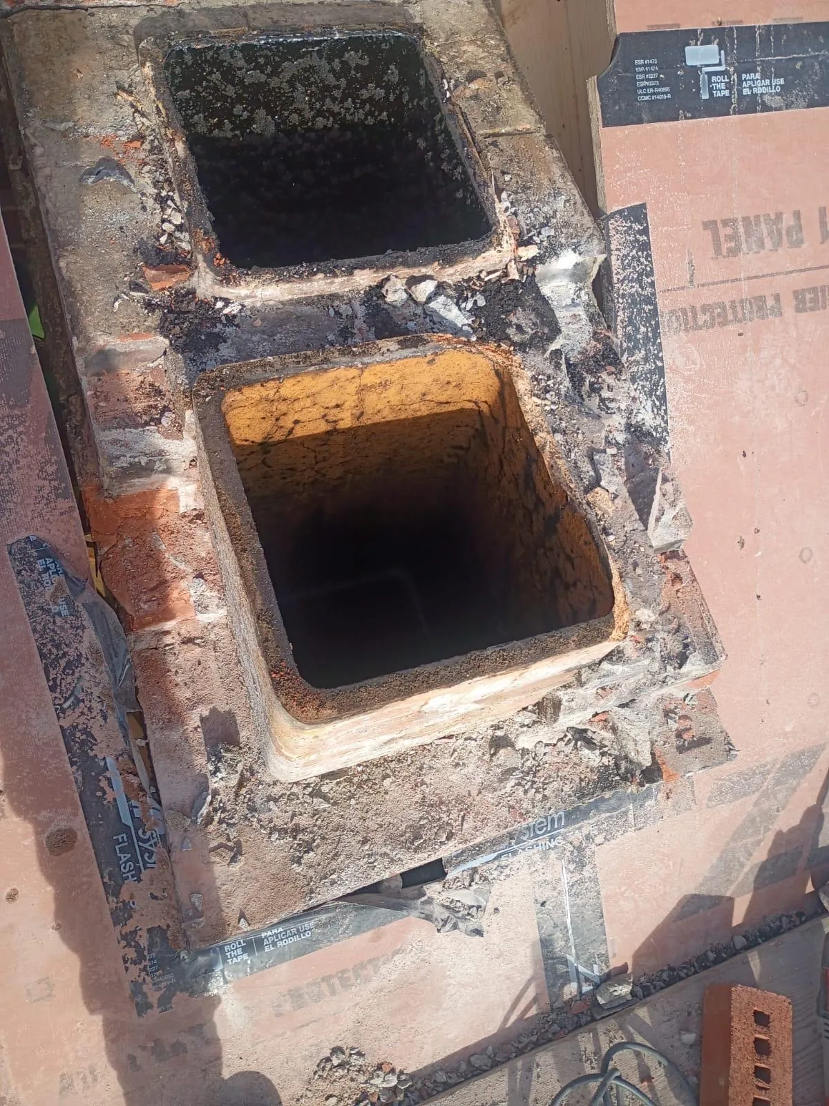 Two old clay chimney flue tiles exposed after the surrounding masonry was removed during a chimney rebuild, with debris and roofing panels around them
