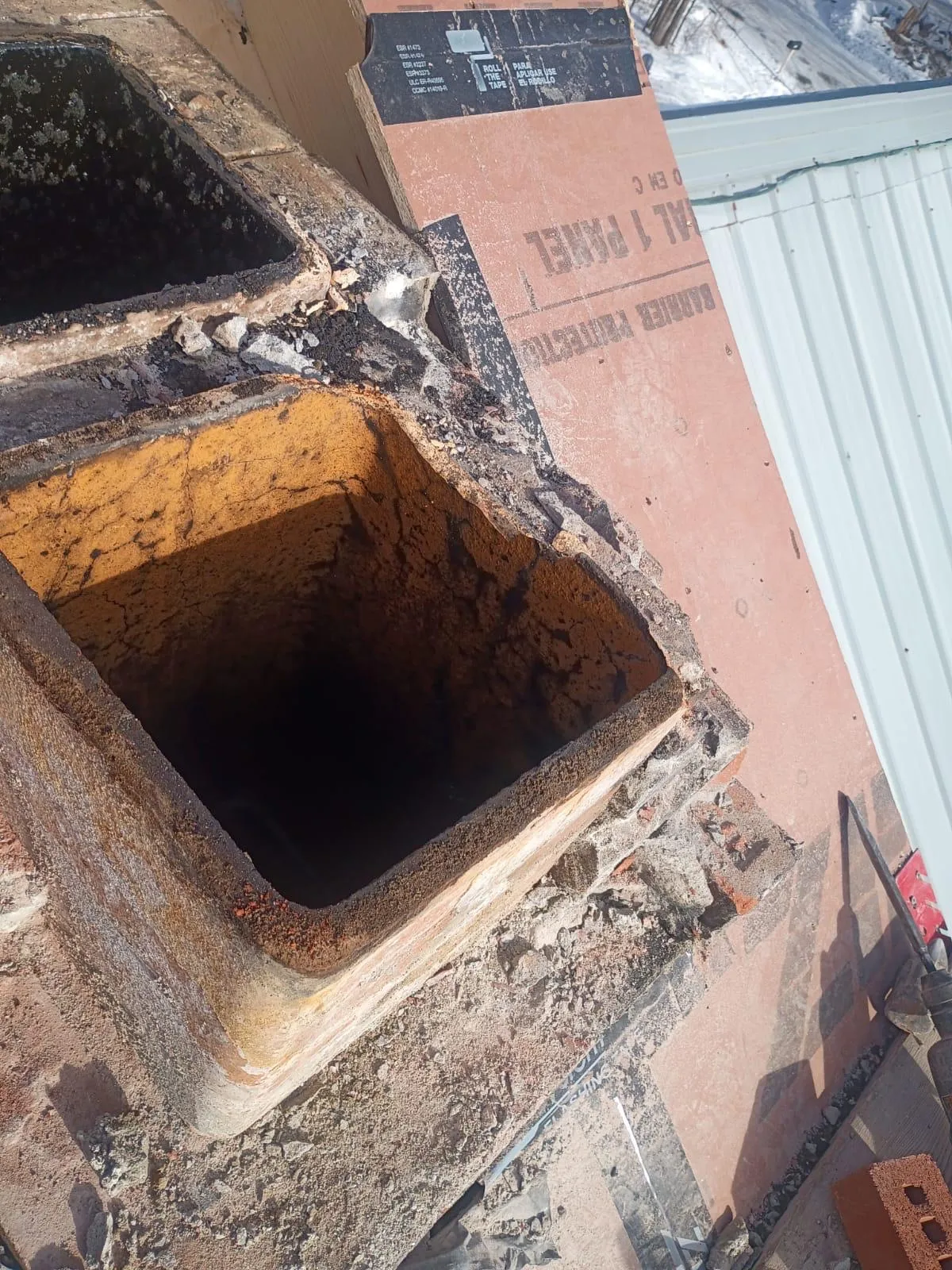 Worn clay flue tile opening on a partially demolished rooftop chimney, photographed in winter with snow visible in the background