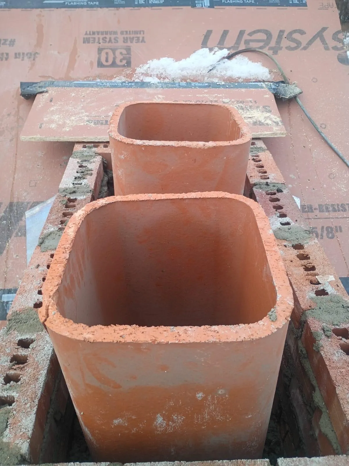Two new clay flue tiles installed in fresh mortar on concrete block during a rooftop chimney rebuild